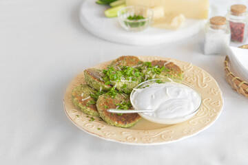 Green zucchini pancakes with sour cream on a plate
