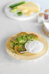 Green zucchini pancakes with sour cream on a plate