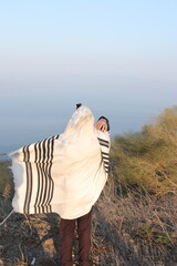 A Jewish man wraps himself in a tallit in prayer in nature
