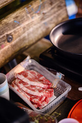 A campsite cooking setup with a non-stick frying pan on a stove, fresh cherry tomatoes, and meat ready to be cooked