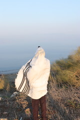 A Jewish man wraps himself in a tallit in prayer in nature