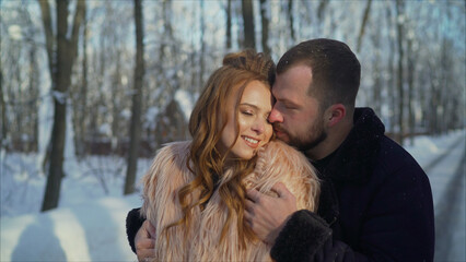 People, season, love and relaxation concept - happy couple hugging and laughing outdoors in winter. A guy and a girl hugging in a winter forest. A girl in a fur coat hugs a guy in the winter forest.