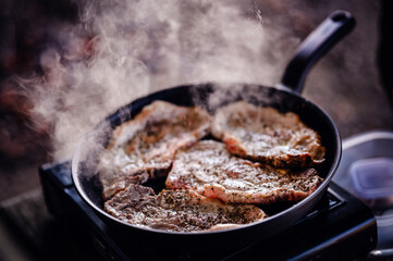 The heat is on as steaks begin to cook on an outdoor portable grill, with smoke curling up...