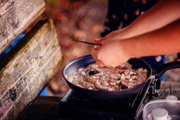 A camper meticulously seasons meat on a grill, demonstrating care and attention to detail in...