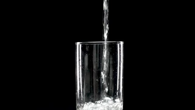 Pour drinking water into a glass of water. Pouring fresh mineral water into a glass, Mineral water in a glass on a black background. Healthy drink concept. Soft Focus, Selective Focus