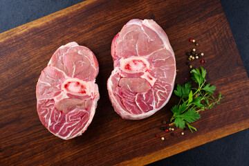 Raw beef leg slice with cross-section marbling with herbs and spices as ossobuco offered as a top view on a wooden design board - obrazy, fototapety, plakaty