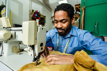 Young male African American tailor sew with a sewing machine in his own atelier