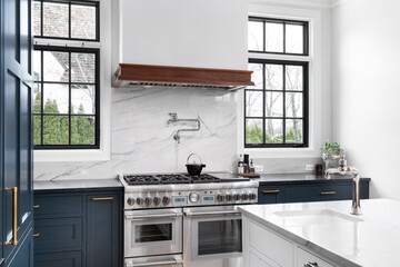 A luxurious kitchen detail with blue cabinets, a stainless steel stove, granite backsplash and...