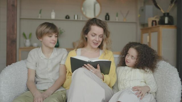 Caring mother reading a story to little daughter and son, family spending time together. Single mum reading bible to teenage siblings brother and sister. Children listening fairytale story with mom