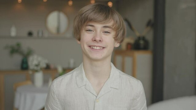 Close up portrait of happy cute Caucasian American male junior student smiling to camera while standing indoor. Joyful smiling boy in good mood. Handsome teenage teenager guy son