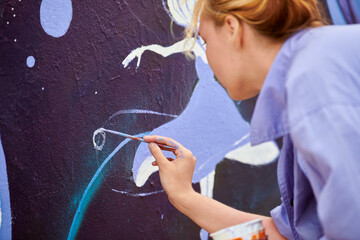 Female painter draws picture with paintbrush on canvas for outdoor street exhibition, close up back...