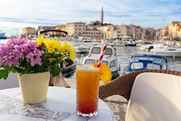 sitting at a table in the harbor of Rovinj with colorful vivid flowers and a tequila sunrise cocktail