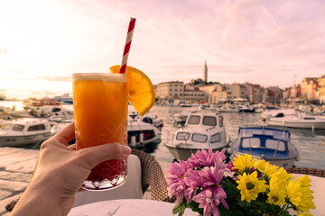 sitting at a table in the harbor of Rovinj with colorful vivid flowers and a tequila sunrise cocktail