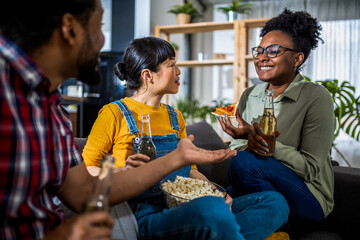Multiethnic group of friends drinking beer and eating pizza and popcorn at home.