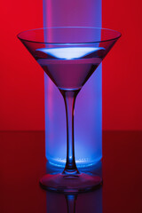 Martini glass filled with blue liquid. Cocktail. Reflective surface. Studio photo isolated on gradient pink background. Martini glass on red background with blue light.