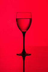 a glass of red wine on a red background with gradient and reflection. Wine glass with a drink. a glass of dry white wine on a red background. 
