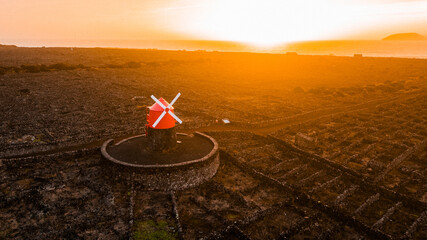 An amazing sunset with a red windmill in the vineyards. The volcanic island of Pico in the Azores....