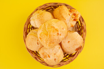 Brazilian cheese bread isolated inside a wooden basket in yellow background in front view