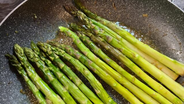 Asparagus, a terrestrial plant, is being cooked in a frying pan. This ingredient is a vegetable and a popular produce in many cuisines
