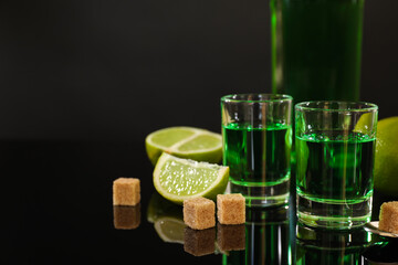 Absinthe in shot glasses, brown sugar, lime and spoon on mirror table, space for text. Alcoholic drink