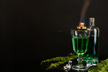 Absinthe, flaming brown sugar, ice cubes and green leaves on mirror table, space for text....