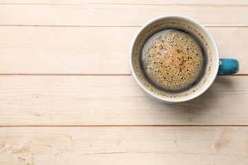 Cup of aromatic coffee on light wooden table, top view. Space for text