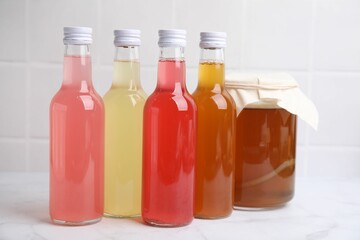 Delicious kombucha in glass bottles and jar on white marble table