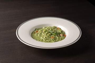 Porridge with spinach and carrots in a white plate on a black background