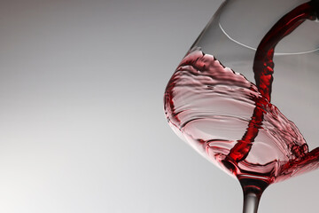 Pouring tasty red wine in glass on light background, closeup. Space for text