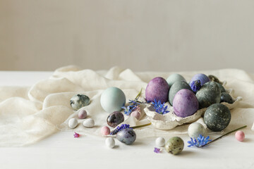 Stylish easter eggs in modern tray, gentle spring flowers and linen cloth on rustic white table....