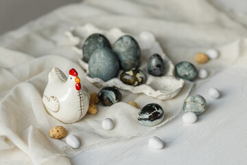 Stylish easter eggs in modern tray and chicken figurine on linen cloth on rustic white table. Easter simple banner. Happy Easter! Natural painted marble eggs still life