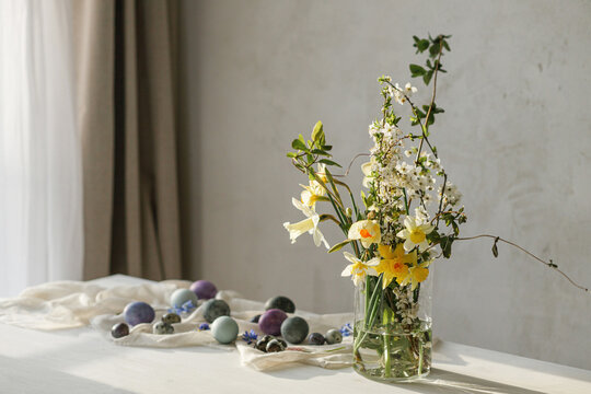 Happy Easter! Stylish easter eggs and spring flowers bouquet on rustic wooden table in rural room. Easter modern simple decor, natural painted marble eggs. Season's greetings