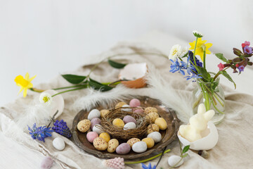 Happy Easter! Stylish easter chocolate eggs in nest, spring flowers, feathers and linen cloth on rustic wooden table. Easter modern simple decoration still life