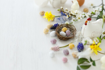 Happy Easter! Stylish easter chocolate eggs in nest, spring flowers, chicken figurine on white rustic wooden table. Easter modern simple banner, space for text. Seasons greetings