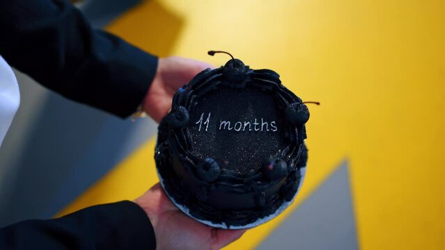 Female hands holding a black sparkling cake with cherries. Celebration of 11 months anniversary. Top view close up.
