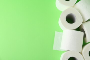 Soft toilet paper rolls on green background, flat lay. Space for text