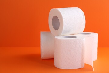 Soft toilet paper rolls on orange background, closeup. Space for text