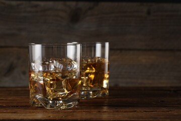 Whiskey with ice cubes in glasses on wooden table, closeup. Space for text