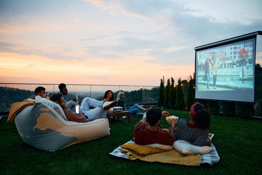 Group of friends relaxing while watching movie on patio at sunset.