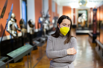 Interested young woman wearing yellow protective face mask viewing collection of medieval knights...