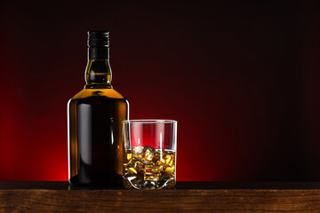 Whiskey with ice cubes in glass and bottle on wooden table, space for text