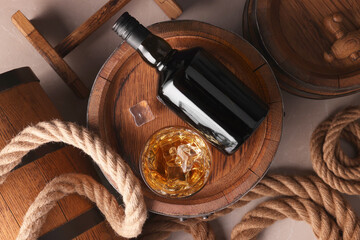 Whiskey with ice cubes in glass, bottle, wooden barrels and rope on grey marble table, flat lay © New Africa