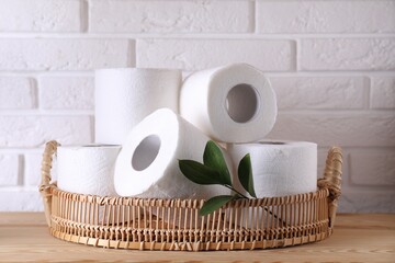 Toilet paper rolls and green leaves on wooden table near white brick wall