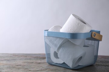 Toilet paper rolls in basket on textured table near light grey wall, space for text