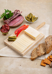 Cheese on a wooden board next to fruit on a beige background