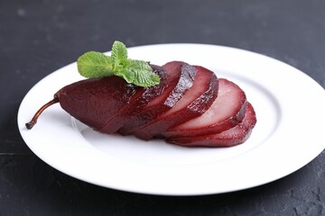 Tasty red wine poached pear and mint on black table, closeup