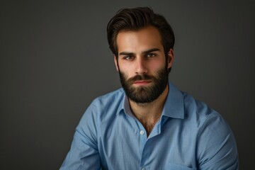 Portrait of confident European businessman with beard and dark hair in blue shirt looking at camera Shot in studio on dark gray background