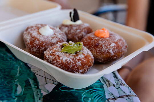 Four malasadas in a plastic take out container, a typical Hawaiian fried pastry dessert, a donut without a hole