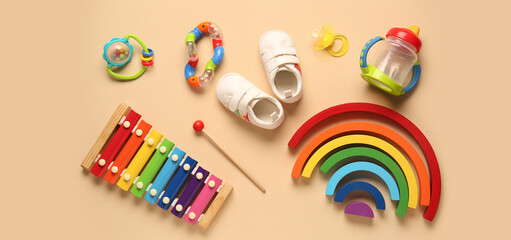 Stylish baby shoes with pacifier and different toys on beige background