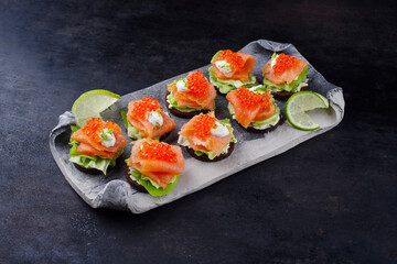 Traditional pumpernickel thaler with smoked salmon and caviar served as a snack on a design tray with copy space